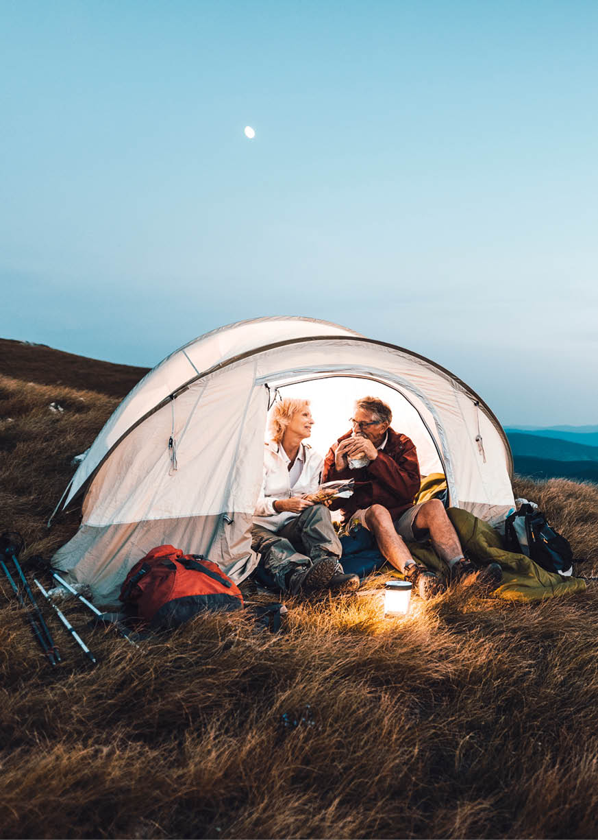 Senior couple camping in the mountains and eating a snack