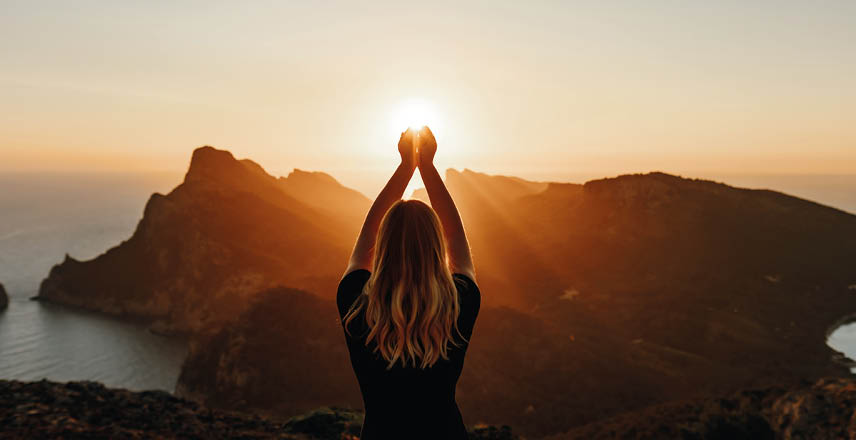 Young woman in spiritual pose holding the light in front of mountains