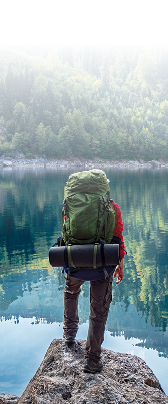 Active tourist with backpack standing at mountain lake and pine wood background