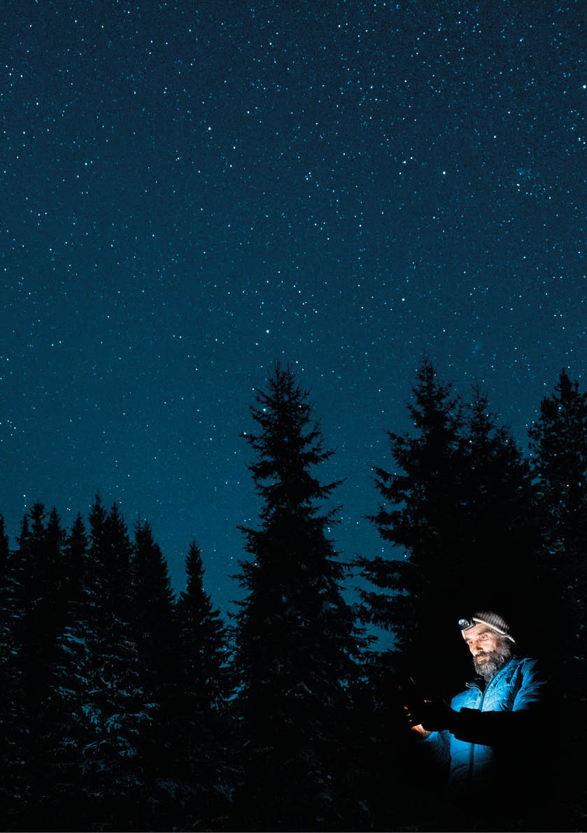 A Cheerful tourist in the Nature at night spending time under the millions of stars in the deep blue sky of the winter snowcapped mountain.