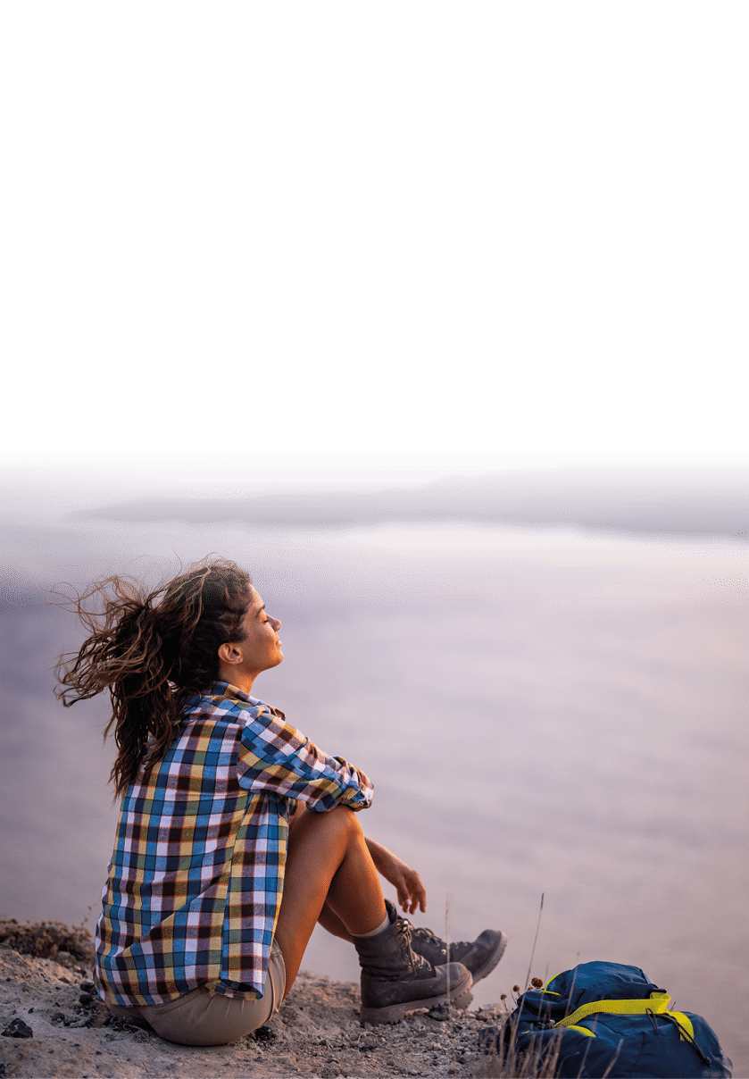 Young female backpacker taking a break after hiking on a hill above the sea at sunset. Copy space.