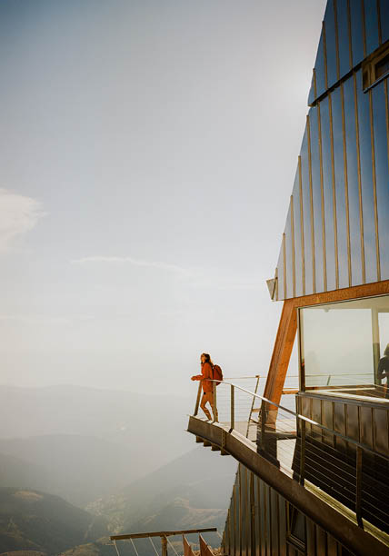 Woman with backpack standing at the balcony of modern alpine shelter in Dolomites. Shot on camera film