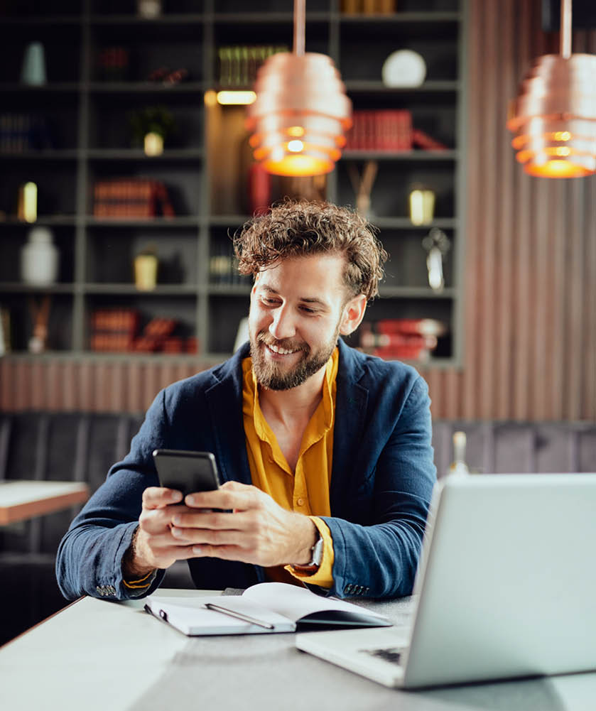 Young Caucasian businessman dressed smart casual using smart phone while sitting in cafe  On the desk is laptop 
