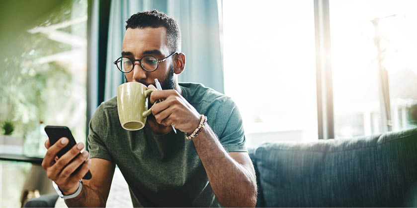 Shot of a young man using a smartphone while going over his finances at home