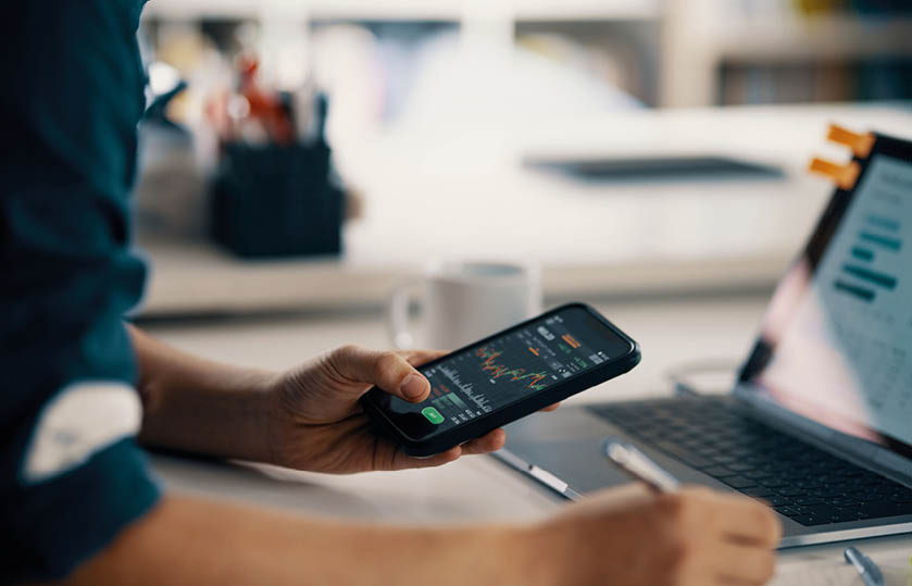 Mid adult man checking financial information on a smart phone while doing his bookkeeping in his home office in Japan. Depicts TradingView financial market chart.